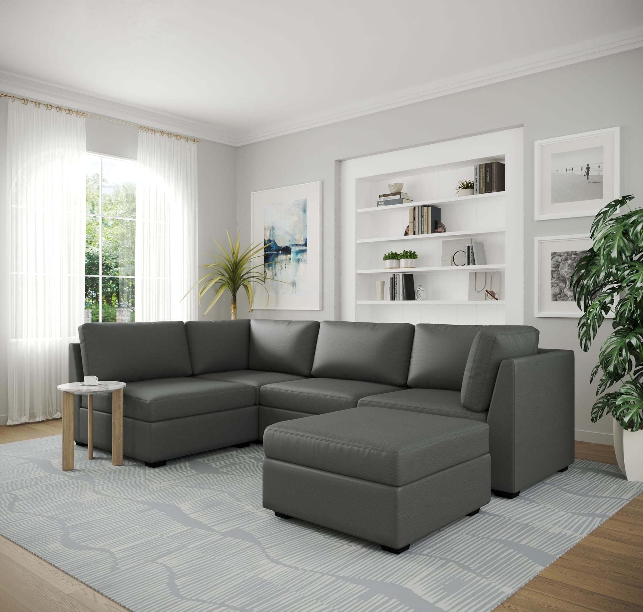 Charcoal leather modular sectional in an L-configuration with a matching ottoman, in the same room with white shelving and sheer curtains